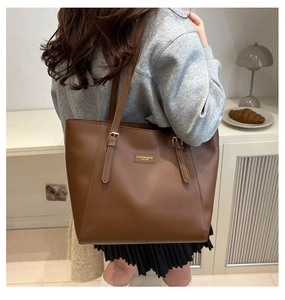 Detail of a brown leather tote bag with decorative adjustable straps and metal buckles