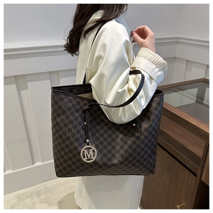 Close-up of brown monogram tote bag with gold M pendant on a shoulder strap