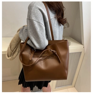Detail of brown faux leather tote bag showing buckle straps and gold fashion logo