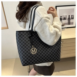 Detail of a black monogram tote bag with gold M charm and grey repeating pattern