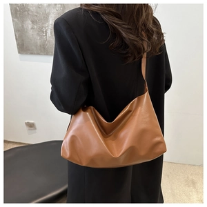 Close-up of caramel brown hobo bag with wide shoulder strap worn over a black blazer