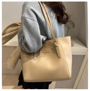 Close-up of a beige large capacity leather tote bag with a fashion logo on the shoulder