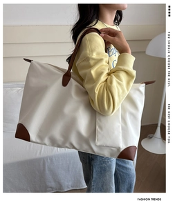 Large cream travel tote bag with brown leather handles worn by a model in a minimalist room