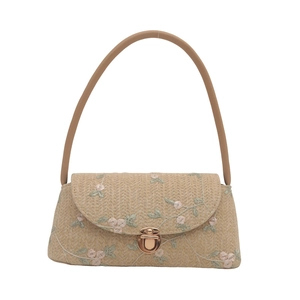 Beige straw woven handbag with pink floral embroidery and metal clasp on white background