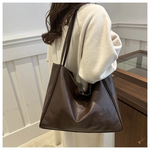 Vue macro d'un grand sac cabas en cuir marron foncé porté par un mannequin en intérieur