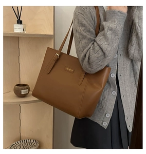 Detail of caramel leather tote bag featuring a brand logo patch and golden hardware