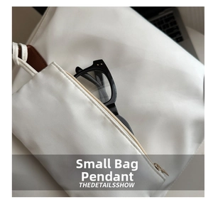 Macro shot of a white nylon mini pouch charm showing eyeglasses storage and gold zipper