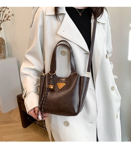 Detailed close-up of dark brown faux leather bucket bag with gold accents on a white coat