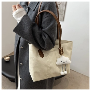 Borsa tote beige con manici in pelle marrone e ciondolo a nuvola soffice su un cappotto grigio