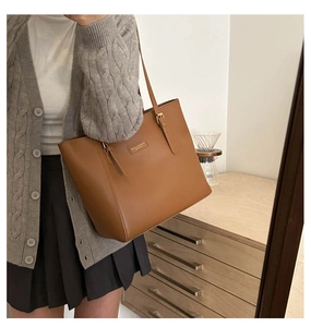 Brown leather tote bag featuring adjustable strap and minimalist gold logo plaque detail