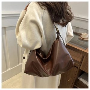 Detail of dark brown leather hobo bag with adjustable gold buckle on a model's shoulder