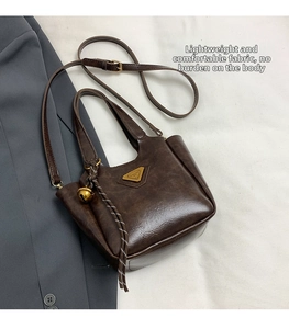 Detail view of dark brown vintage faux leather tote bag with metallic logo and bell charm