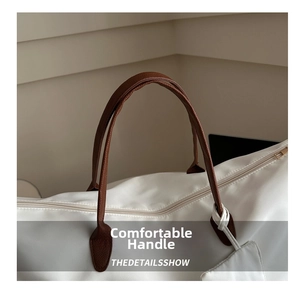 Detail showing the brown leather handle and zipper on a large white travel bag