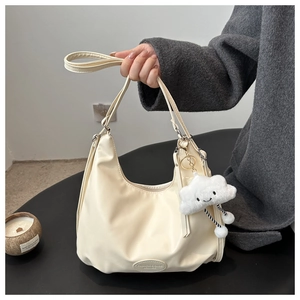 Detail of creamy hobo bag with moon shape, brand logo patch and plush cloud pendant