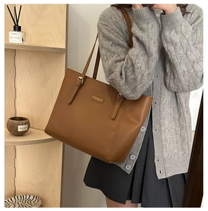 Close-up of brown leather tote bag showing adjustable strap and fashion metal logo