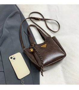 Detailed view of the brown retro bucket bag with a metal logo plate next to a smartphone