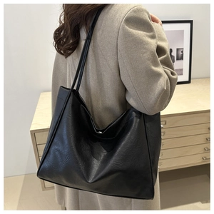 Détail d'un grand sac cabas noir porté par un mannequin dans un décor minimaliste