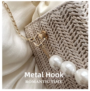 Detail of straw woven bag featuring golden hardware hooks and elegant pearl charm accents