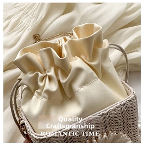 Detail of cream drawstring bucket bag featuring straw base and golden chain strap