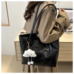 Detailed view of a large black leather tote bag with a cute white cloud plush charm