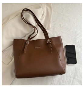 Detail of dark brown leather tote bag with gold hardware and logo on white fabric