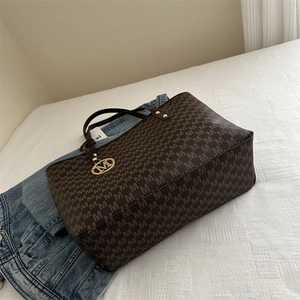 Classic dark brown monogram tote bag with leather handles on a casual white fabric background