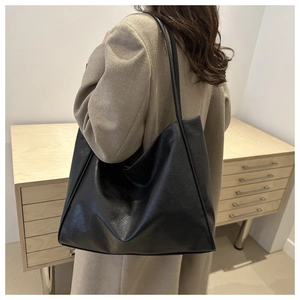 Détail de la texture d'un sac cabas noir porté sur un manteau d'hiver beige chic