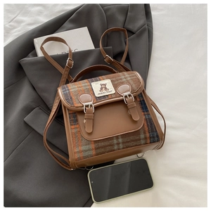 Detailed view of the brown plaid backpack featuring faux leather straps and vintage patches