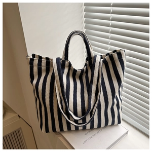 Detail view of a black and white striped canvas tote bag resting on books near window light