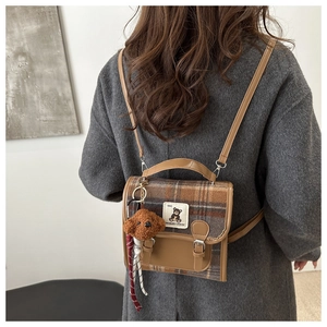 Detail of vintage plaid backpack with leather flap and plush bear charm on model back