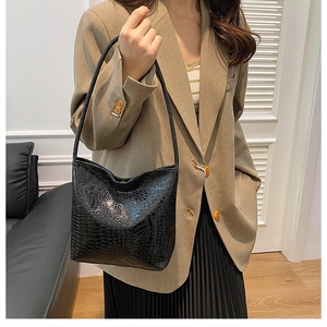 Detail of black crocodile-embossed bucket bag worn with a beige blazer for office look