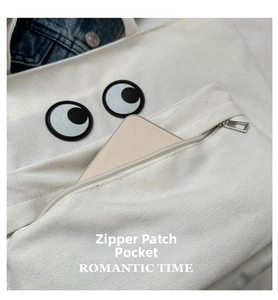 Close-up of canvas tote bag showing the functional zipper pocket with eye embroidery