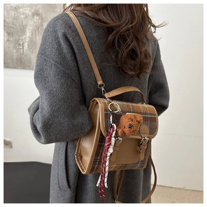 Detail of vintage brown plaid backpack featuring faux leather trim and bear charm