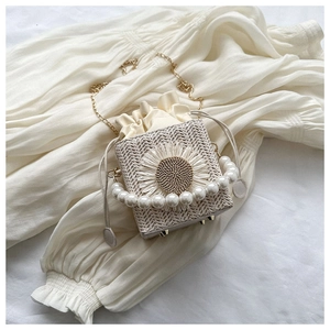 Detail of square straw bag with white daisy decoration, pearl handle and golden chain