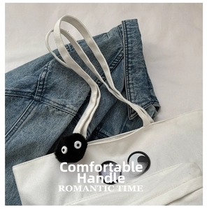 Detail of white canvas tote bag with black fuzzy pompom and large cartoon eye patches