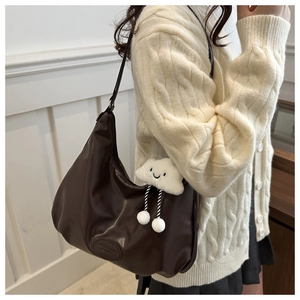 Detail of dark brown leather tote with a cute white cloud plush charm and embossed logo