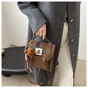 Detail of plaid bag with brown leather accents and cute teddy bear charm accessory