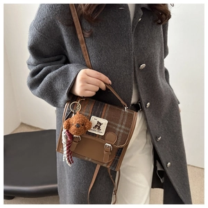 Close-up of retro plaid crossbody bag with teddy bear charm on wool coat background