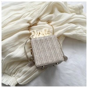 Detail of woven straw bucket bag with gold chain strap, pearl charm and metal feet