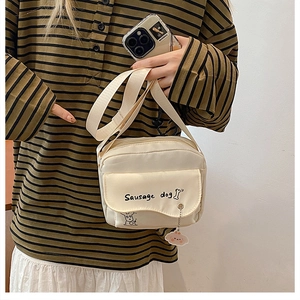 Detail van crème canvas crossbodytas met schattige hondenprint en een pluche hanger