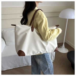 Model wearing a large cream tote bag with brown leather corners and zipper detail