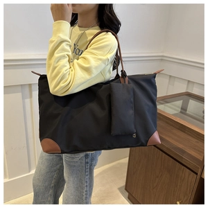 Detail of a black nylon tote bag with brown leather handles and a matching mini pouch charm