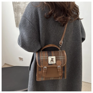 Detail of vintage brown plaid backpack with adjustable leather straps and bear patch