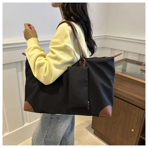 Close-up of a large black nylon tote bag with brown leather details on a model shoulder