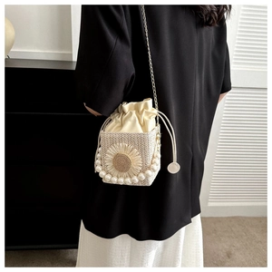 Detailed straw bucket bag with pearl handle and 3D floral accent against a dark suit