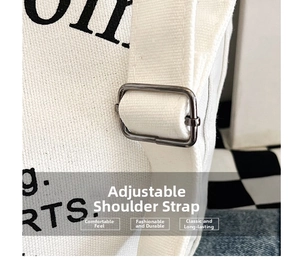 Detail of adjustable metal buckle on off-white canvas shoulder strap with black lettering