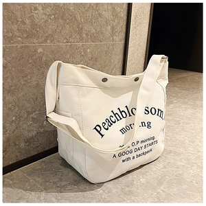 Detailed view of cream canvas tote bag with black letter print and metal hardware