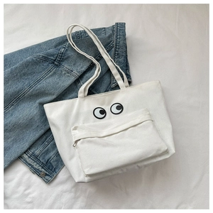Detail of white canvas tote bag with embroidered eyes and zipper pocket on denim