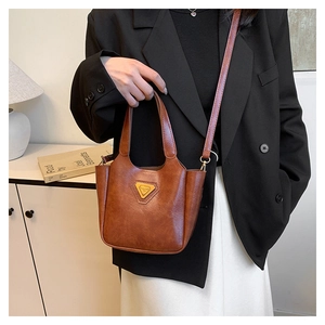 Brown vintage PU leather bag with triangular metal plaque worn by a model in a modern room