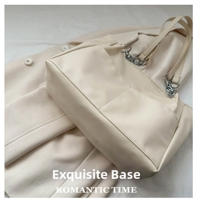 Detail of cream leather tote bag featuring refined stitching and metal chain decor